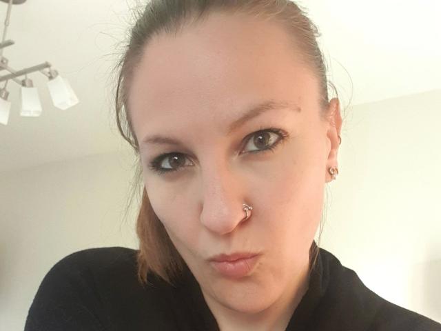 Swissmiss88-hot has a nose piercing, brown eyes, and pouty lips. She's wearing a black shirt and has brown hair in a ponytail. She's also wearing small earrings.