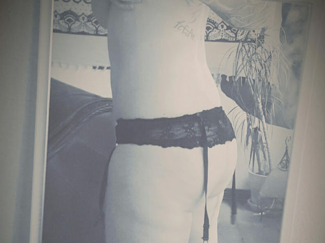 NoireEtoile-hot's bare back and black lace garter butt, showing a tattoo on her right side, with a mirror reflection capturing her from the side.