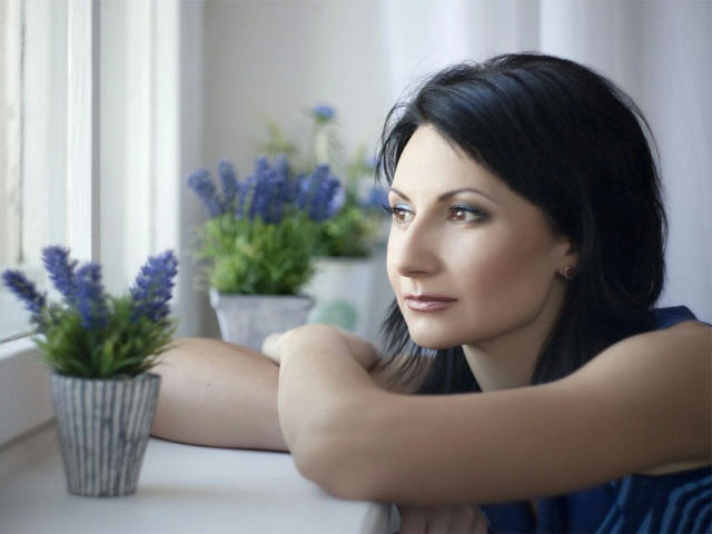PinkSpark-hot with dark hair, brown eyes, and a slight smile, leaning on a window sill, arms crossed, looking outside, with purple lavender in gray pots to her left.