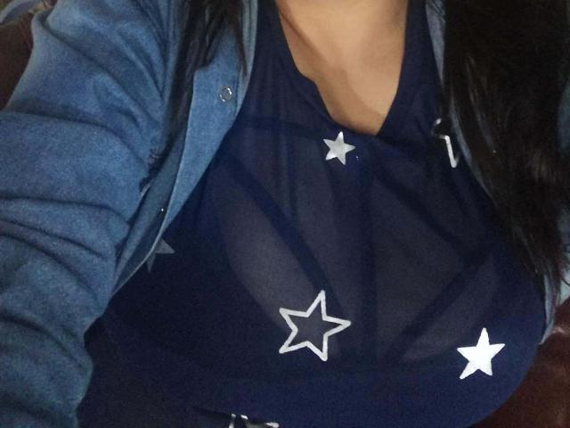 ZafiRouge's tits are visible through a sheer navy blue top with white star patterns, covered by a blue button-up shirt. Her dark hair is partially visible.