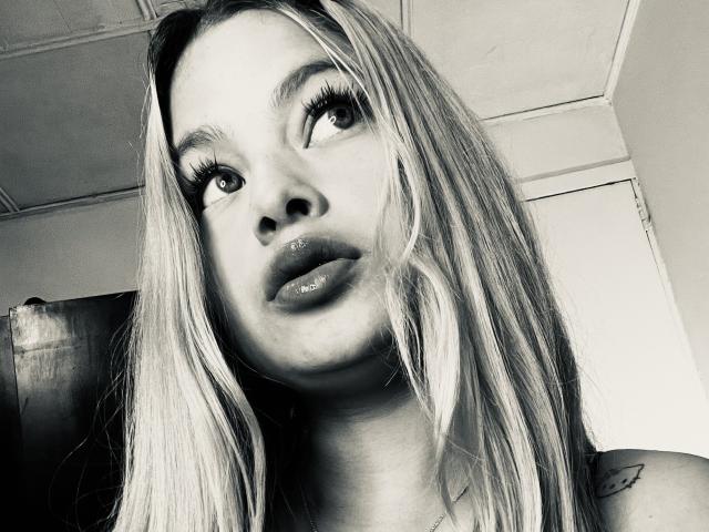 ShantalSummer heeft glanzende lippen, lang blond haar en dikke wimpers, en ze kijkt op met een lichtelijk nieuwsgierige uitdrukking. Haar neus is recht en ze heeft een kleine tatoeage op haar schouder..