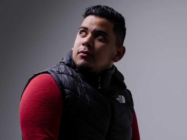 DmitriIvanov has dark hair, a slightly pensive expression, and wears a black puffy vest over a red long-sleeve shirt. His chest is prominent.