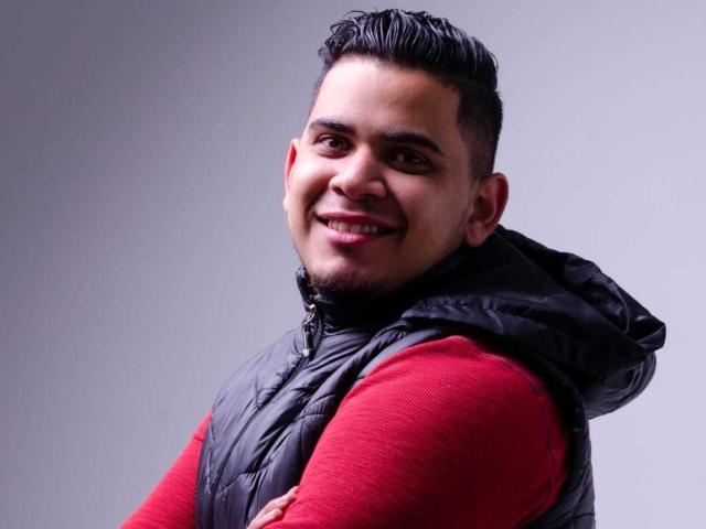 DmitriIvanov with short, dark hair, puffy black vest, red sweater, smiling, arms crossed, light skin, slightly chubby, looking at camera, gray background.