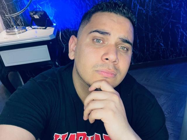 DmitriIvanov, a chubby dude with short dark hair and green eyes, pouts his lips, resting his chin on his hand, wearing a black t-shirt, in a selfie.