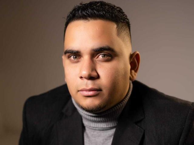 DmitriIvanov has a serious face, short black hair, brown eyes, and a light skin tone. He's wearing a black suit jacket over a grey turtleneck.