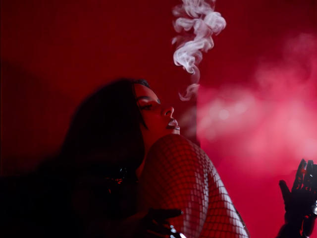 ArtemisaStone with dark hair, smoking, eyes closed, wearing a red-checkered shirt, red light, white smoke, black gloved hand, sensual, relaxed, cigarette in mouth, moody atmosphere.