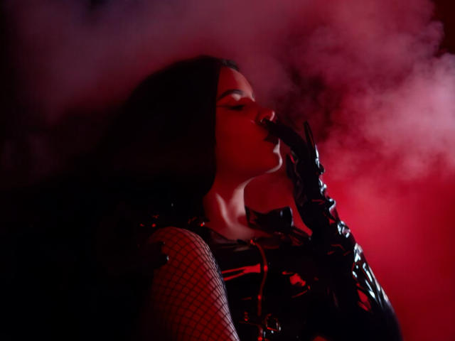 ArtemisaStone with dark hair, red glow, and black latex gloves, sensually sucking fingers, wearing fishnet sleeves and glossy black top, surrounded by red mist.