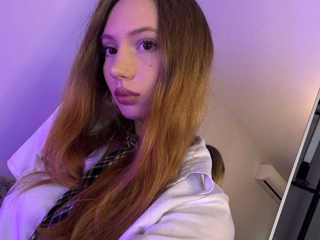 ElfinVibes with long brown hair, pouty lips, and a white shirt, wearing a green plaid tie, looking directly at the camera with a slightly serious expression.