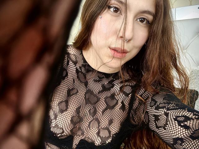 AmberlStha, con lunghi capelli castani, indossa una maglia nera in pizzo e rete, che lascia intravedere i suoi seni attraverso il disegno, ha un anello al naso e le labbra leggermente socchiuse, in un selfie..
