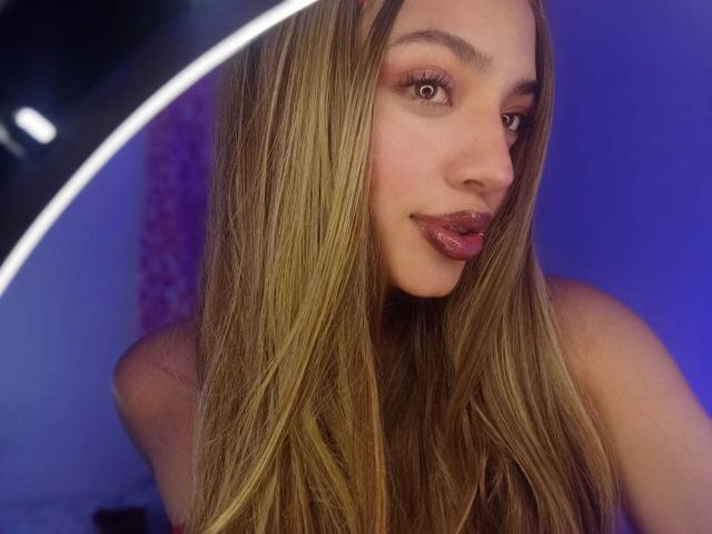 IvyCors has long, straight brown hair, brown eyes, and shiny pink lipstick. She's looking to the side with a slight smile. A circular light is in the top left.