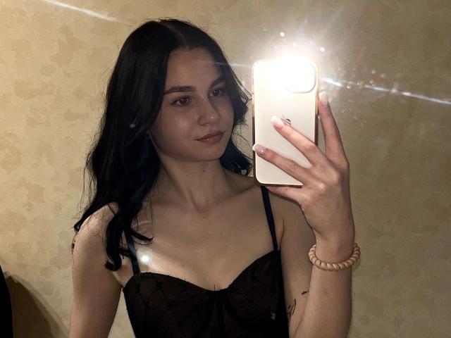 Treat-hot with black hair, wearing a black lace top, taking a mirror selfie with a white phone, showing small tits and a light skin tone.