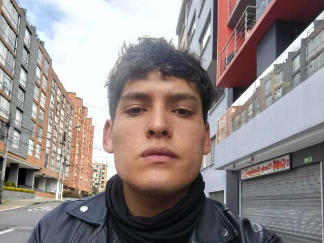 DiegoBiker has curly black hair, light brown skin, and a neutral expression. He's wearing a black leather jacket and a black shirt. Urban street background.