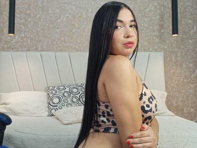 AliceSmity with long black hair, wearing a leopard print top, showing her back and looking over her shoulder with red lipstick, her hands on her ass, red nails.