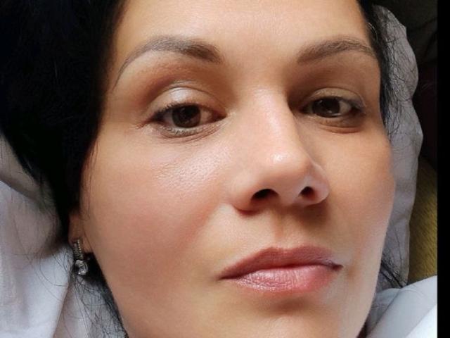 DayanaSins a un visage lisse, de couleur marron clair, avec un maquillage discret, des yeux marron foncé et un léger sourire. Elle porte de petites boucles d'oreilles au design simple..