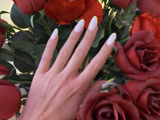 AlicePrings' hand with white nails and yellow tips, fingers spread, touching red roses. Her hand has a light skin tone and visible veins. Roses fill the background.