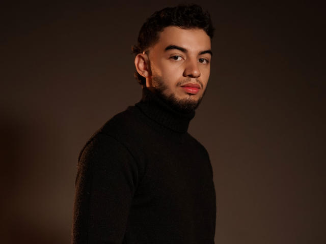 MichaelMagno has curly dark hair, a beard, and is wearing a black turtleneck. He's looking slightly to the side with a subtle, confident smile.