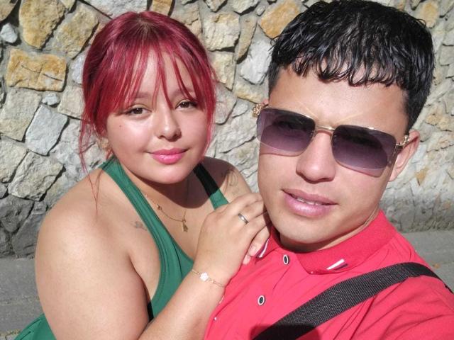 LoveAndMadness with red hair, green dress, and cute smile, next to a guy with black hair, red shirt, and dark sunglasses, holding her hand.