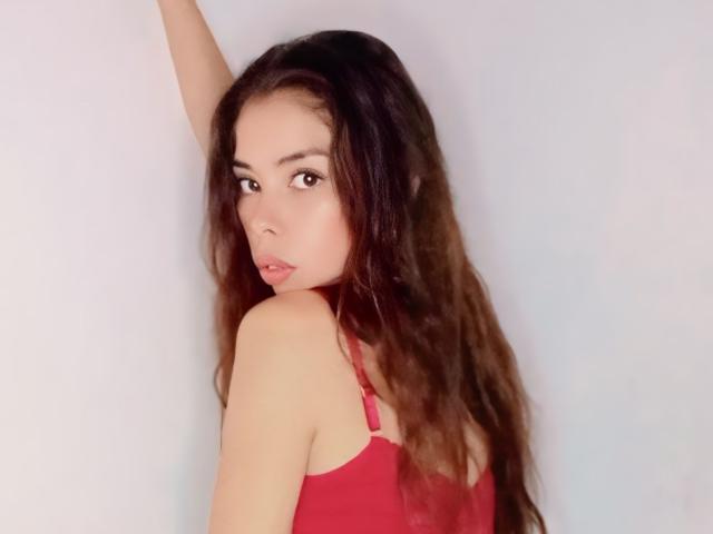 AyeBeauty with long brown wavy hair, red tank top, looking back over shoulder, right arm raised, sexy, pale skin, brown eyes, slightly parted lips, soft light.