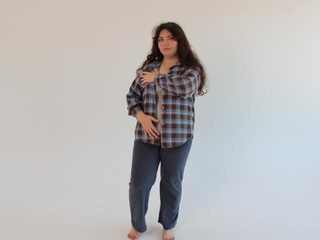NeonilaLisova, barefoot, long dark hair, plaid shirt, dark pants, arms crossed, hand on belly, standing, neutral expression, white background, casual, slightly overweight, confident.