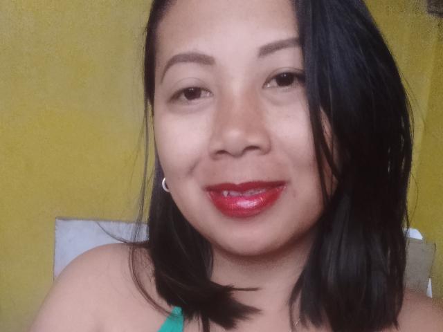 SarahFontaineX has dark brown hair, red lipstick, small hoop earrings, and a green top, smiling at the camera with slightly parted lips.
