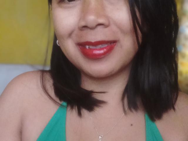 SarahFontaineX has medium brown skin, black shoulder-length hair, red glossy lips, green halter top, small silver necklace, and a slight smile, showing a cute, sexy look.