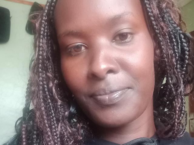 EllieNelle's face with brown braided hair, glossy brown lips, and a subtle smile. Her dark skin has a smooth texture, and she's wearing a black shirt.
