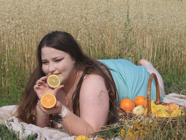 DaniellaGraceZZ, chubby with long brown hair, eating orange halves, lying on blanket, wearing blue dress, orange and apple basket, wheat field, summer, white watch, relaxed, happy.
