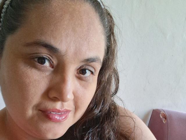 AlyceDina's face with brown wavy hair, brown eyes, slightly parted pink glossy lips, and a light brown skin tone, wearing a hairband, in a selfie.