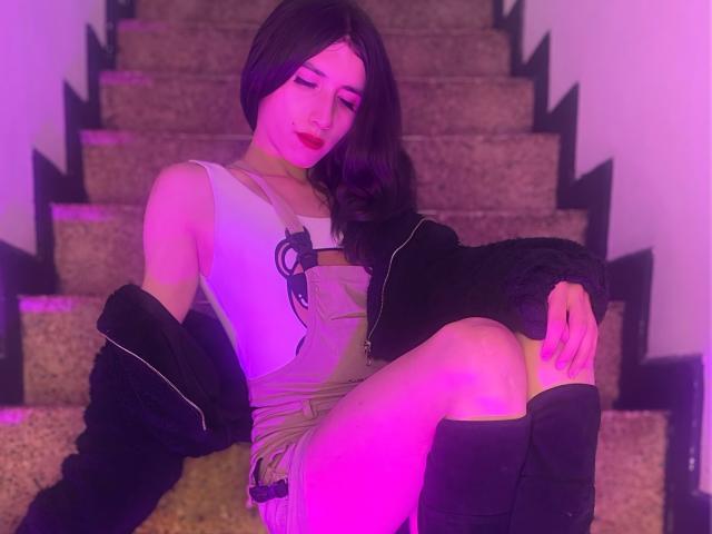HiromiHotX with purple-tinted skin, dark hair, red lipstick, wearing a dress, black jacket, and knee socks, sitting on carpeted stairs, legs crossed, looking down, sexy.