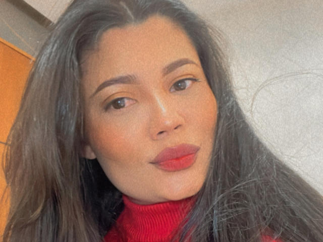 Maryorieth's face, with long brown hair, subtle makeup, and red lipstick, wearing a red turtleneck. Her brown eyes are slightly upturned, and she has a gentle smile.