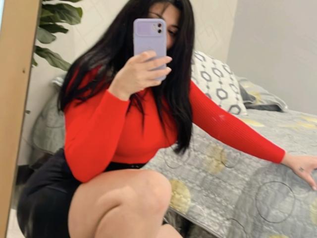 Maryorieth with long black hair, red long-sleeve top, and black skirt, taking a mirror selfie, showing her ass and thigh, holding a purple phone, in a bedroom.
