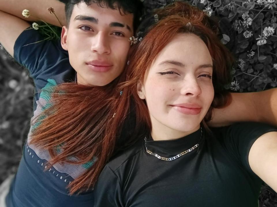 AdrianyCamila con i capelli rossi e AdrianyCamila con i capelli scuri, sdraiate, sorridenti, che indossano magliette nere, la mano di AdrianyCamila nei capelli di AdrianyCamila, entrambe che guardano la fotocamera..