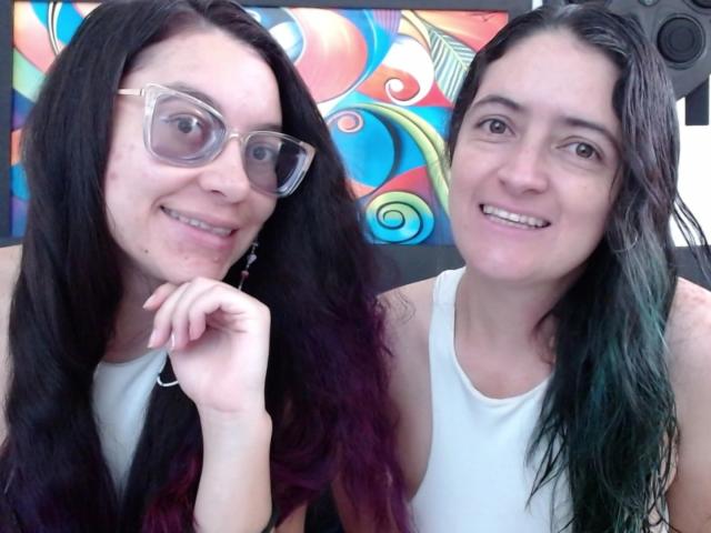 LunaVenus has dark hair, wears glasses, and smiles with her hand near her mouth. LunaVenus with green-tinted hair, white tank top, smiles. Both have visible tits.