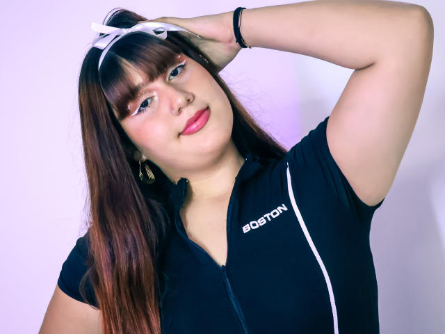BibiCruz with brown hair, wearing a black sports zip-up, white headband, pink lipstick, and black bracelet, smiling, hand in hair, exposing her cute, chubby ass.