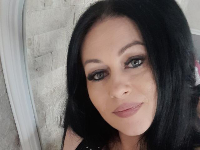 Sellhena tiene el cabello negro, ojos verdes y está sonriendo con labios rosados. Lleva delineador de ojos oscuro y una blusa negra. Su trasero no es visible..