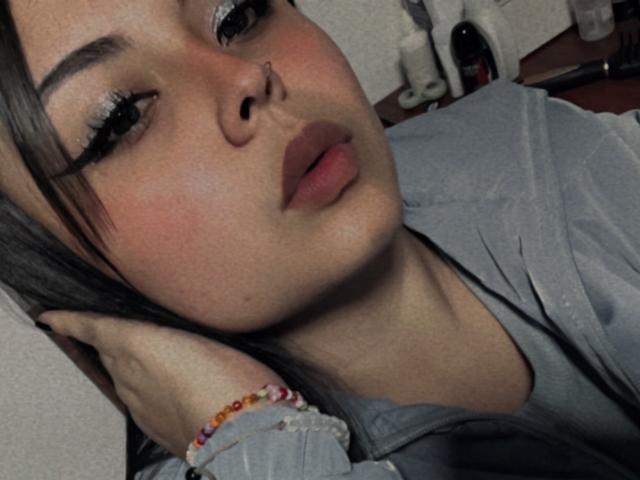 ViolethhLee has a cute nose ring, thick eyelashes, and slightly pouty lips. She's wearing a grey shirt with a colorful bracelet on her wrist.