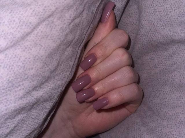 Barberry's hand with long, glossy pink nails is gripping a gray, textured fabric. Her skin is pale, and the fingers are slightly curled.