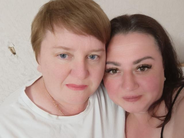 MollyAndJane with short red hair and blue eyes, wearing a white shirt, stands beside MollyAndJane with dark brown hair and green eyes, wearing a black top.