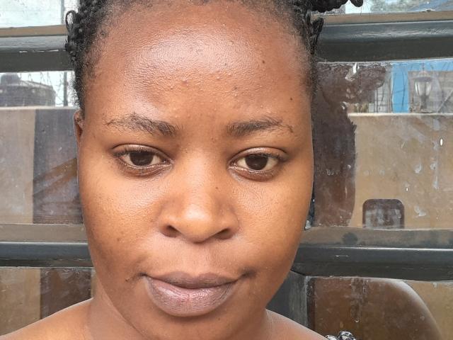 QueenBoobby has medium brown skin, small dark eyes, and curly black hair. Her face is slightly sweaty, with a subtle smile, and she's wearing no clothes.