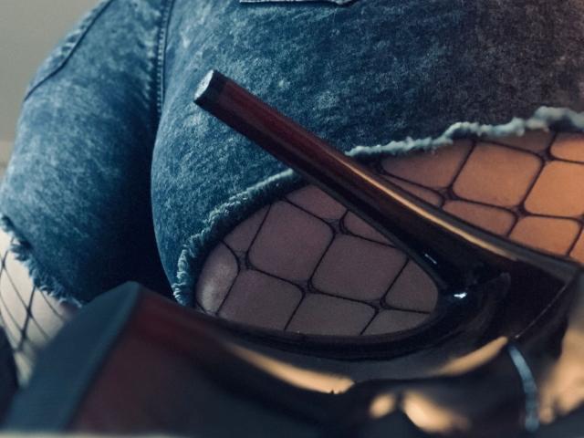 LauraSinnerX's tits are covered in a torn, blue denim shirt with fishnet fabric over her face, holding a dark brown, shiny, metal pipe near her mouth.