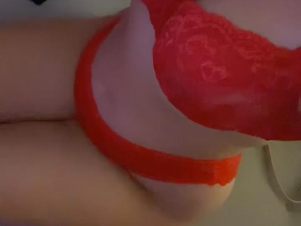 Albaa69's red lace bra and matching red lace panties are visible, showing her pale skin and her butt in the foreground. The image is a slightly blurred, angled shot.