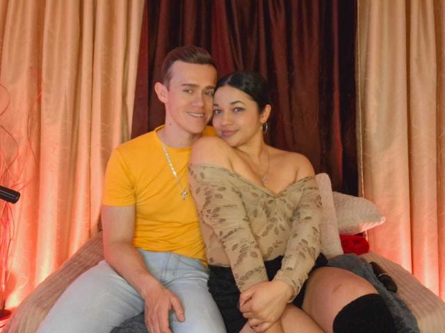 JenAndPatrick, a cute couple, sitting together. Patrick, in a yellow tee and jeans, has a muscular build and short brown hair. Jen, in a floral off-shoulder top, shows her tits.