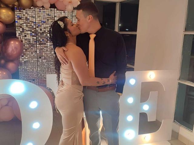 JenAndPatrick kissing, she's in a tight, beige, backless dress showing her ass, he's in a black shirt and jeans, holding her waist, in a softly lit room.