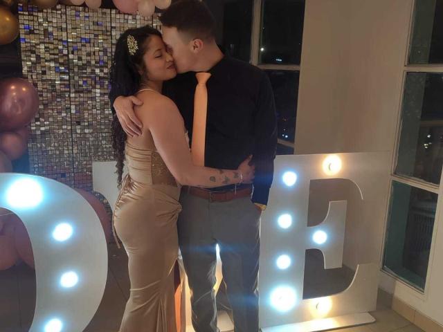 JenAndPatrick are kissing, she's wearing a shiny beige dress with her ass hugged, he's in a black shirt with a neon tie, his hands on her butt.