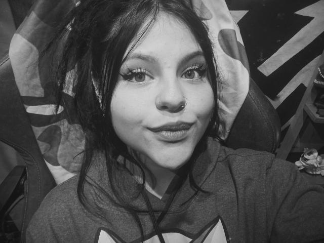 Ein Schwarz-Weiß-Selfie von Sophie Hill mit dunklem, zerzaustem Haar, Nasenring und einem leichten Lächeln, die einen Hoodie trägt, mit sichtbaren Wimpern und einem leichten Schmollmund, die direkt in die Kamera schaut..