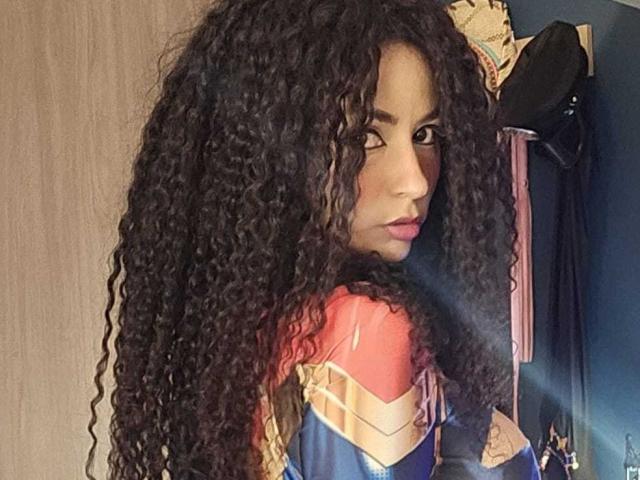 SexyKonnyX with huge curly black hair, looking over shoulder, wearing a Wonder Woman costume, showing a strong, sexy face, and a subtle, confident smile.