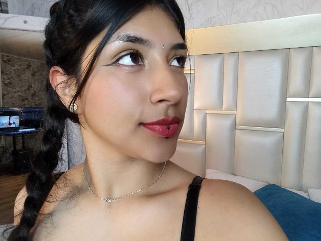 TatianaMorelli has a cute face with a black braid, red lipstick, and a nose ring. She's wearing a black strap, and her tits are slightly visible.