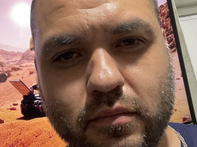 EhdgherMrLA's face, with a serious expression, short beard, and brown eyes, is in the foreground of a Martian landscape photo, featuring a small robot on the left.