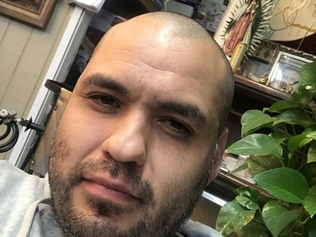 EhdgherMrLA has a bald head, light brown skin, thin beard, and small nose. His eyebrows are slightly raised and he's looking at the camera with a slight smile.