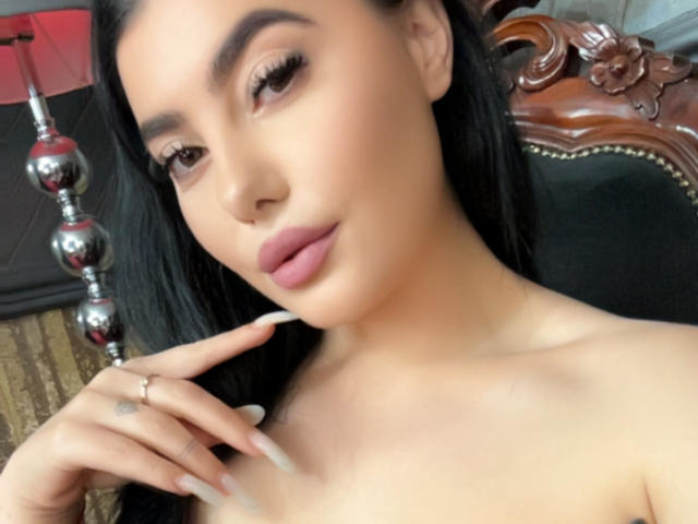 MelissaGlow with long black hair, light brown skin, full pink lips, and dark eyebrows, showing off her tits with manicured nails, wearing a ring on her finger.